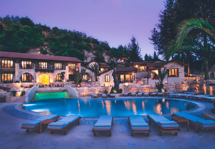 Luxurious resort poolside at twilight with illuminated pool, lounge chairs, and a multi-level traditional building nestled against a hillside.