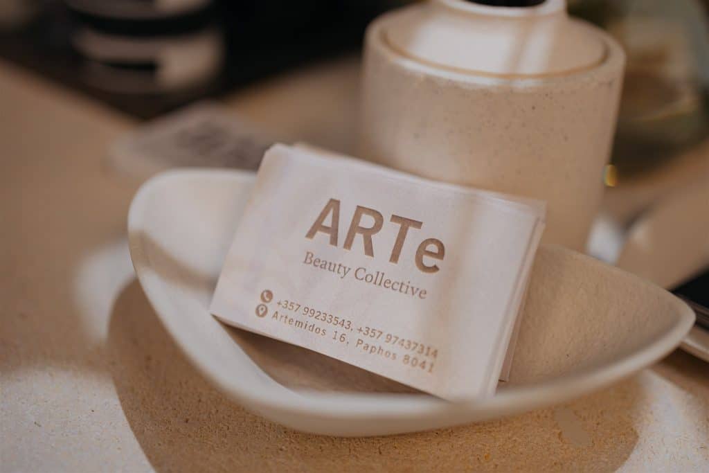 A close-up photo of a business card for "arte beauty collective" placed in a white ceramic bowl on a tabletop, with blurred kitchen items in the background.