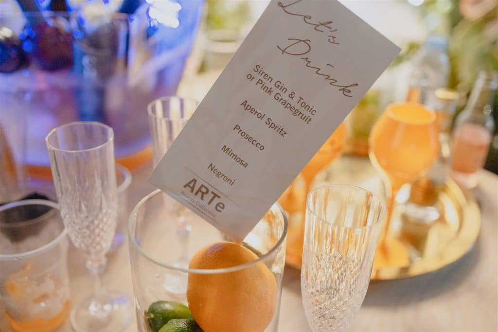 An elegant cocktail menu titled "let's drink," featuring drink options such as gin & tonic and aperol spritz, amidst a festive table setting with empty glasses and citrus fruits.